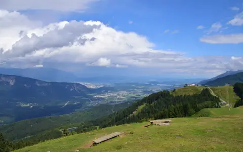 Symbolbild: Breathtaking view from Arnoldstein, Austria showcasing lush green valleys, forests, and rolling mountains under a bright blue sky.